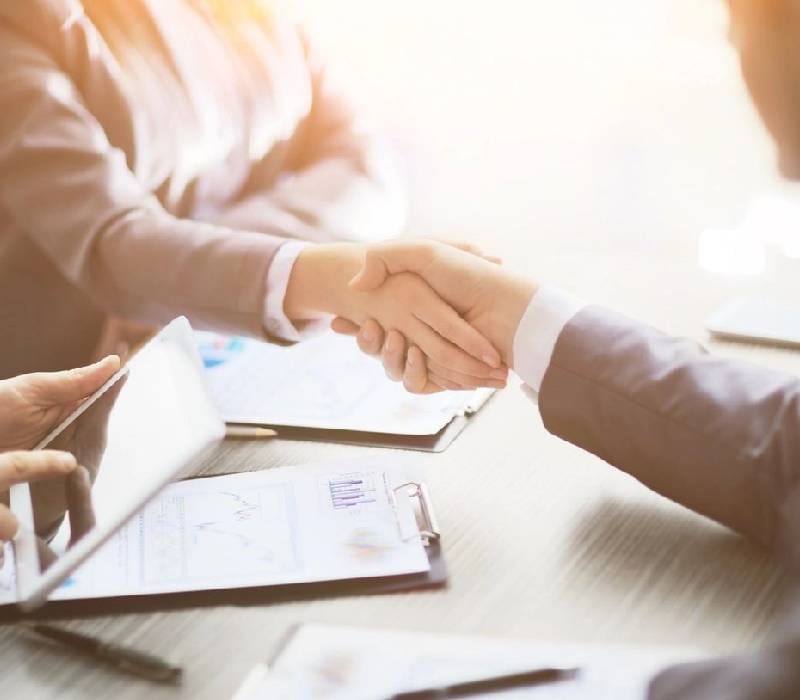 Two people shaking hands over a table.