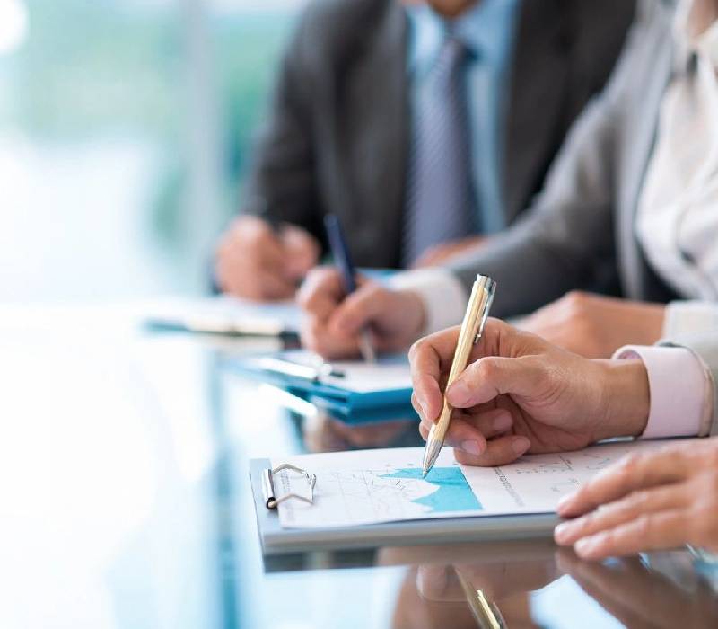 A group of people sitting at a table with pens and paper.