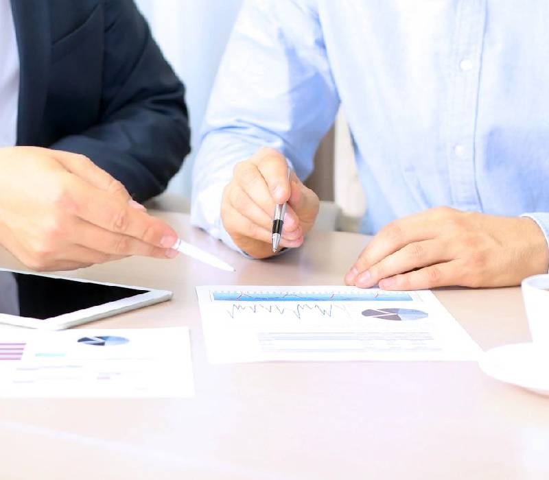 Two people sitting at a table with papers and one holding a pen.