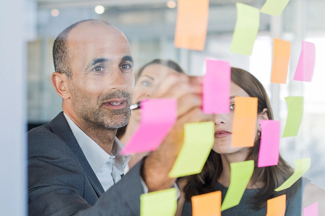 A man and woman are writing on sticky notes.